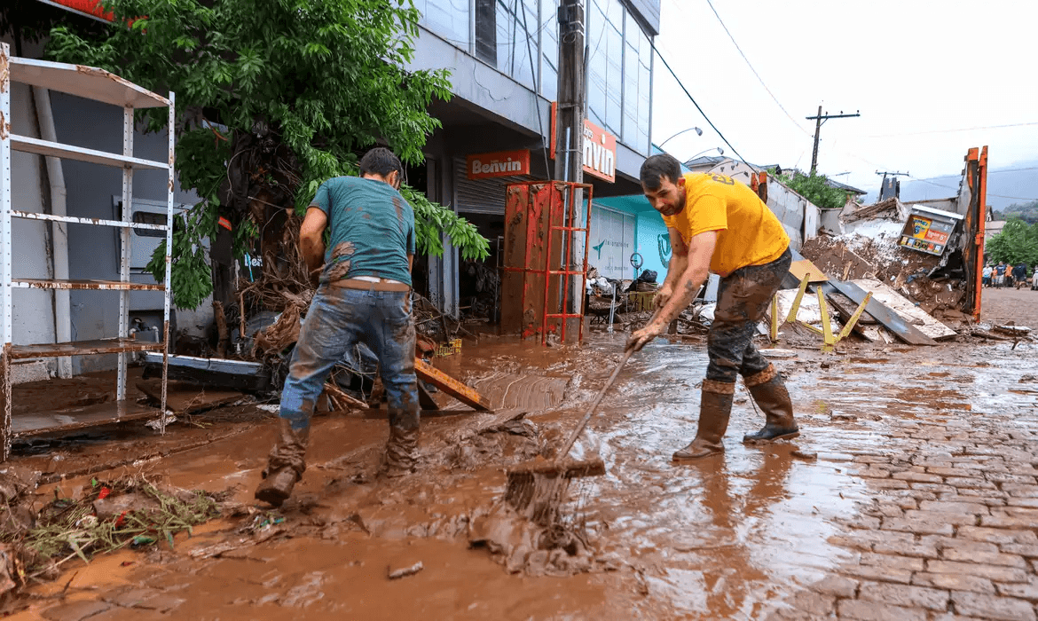 Foto de pessoas limpando ruas destruídas no Rio Grande do Sul